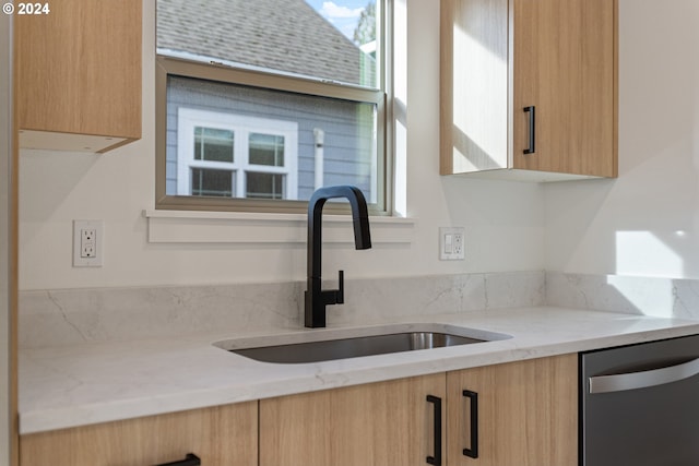 kitchen featuring stainless steel dishwasher, light stone countertops, sink, and light brown cabinetry