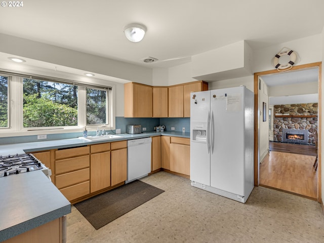 kitchen with light brown cabinets, white appliances, a stone fireplace, sink, and light hardwood / wood-style floors