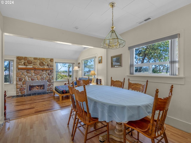 dining room with lofted ceiling, light wood-type flooring, a fireplace, and an inviting chandelier