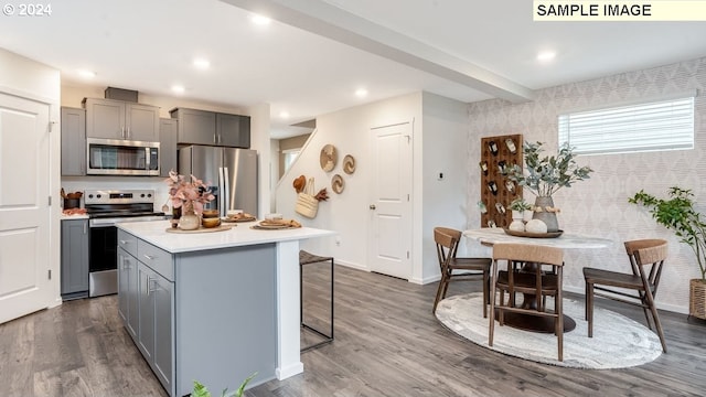 kitchen featuring stainless steel appliances, dark hardwood / wood-style flooring, a breakfast bar area, gray cabinets, and a kitchen island