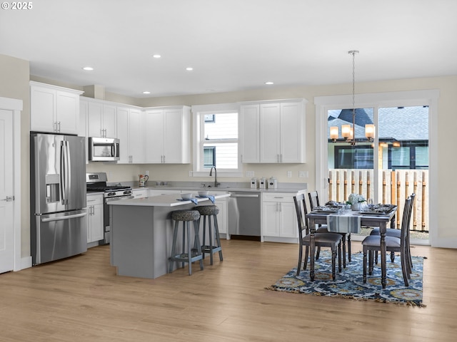 kitchen with a sink, a chandelier, light wood finished floors, appliances with stainless steel finishes, and a kitchen island