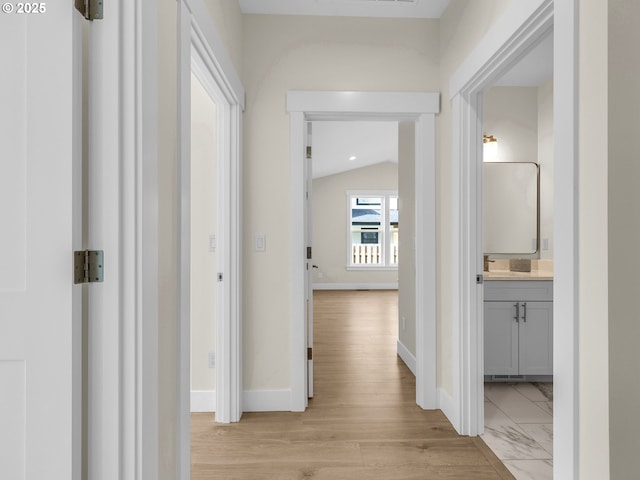 hall with vaulted ceiling, baseboards, and light wood-type flooring