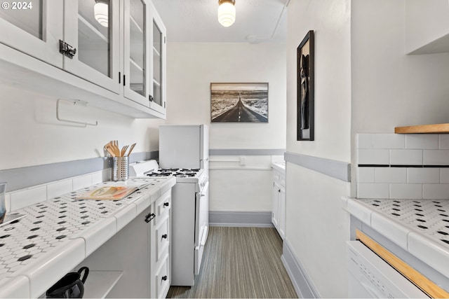 kitchen with tasteful backsplash, white cabinetry, glass insert cabinets, baseboards, and white gas range