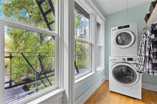 laundry area featuring laundry area, baseboards, stacked washer and clothes dryer, and wood-type flooring