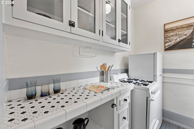 kitchen with tile countertops, baseboards, white range with gas cooktop, glass insert cabinets, and white cabinetry