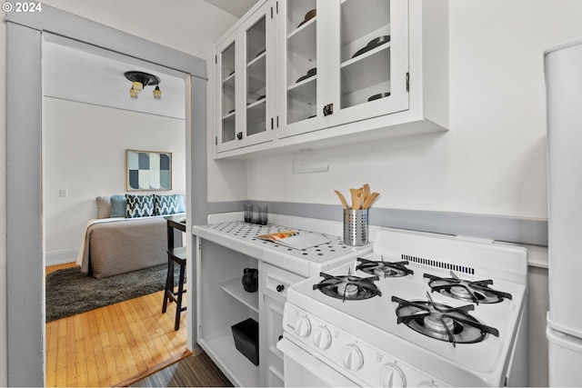 kitchen with glass insert cabinets, white gas stove, tile countertops, wood finished floors, and white cabinets