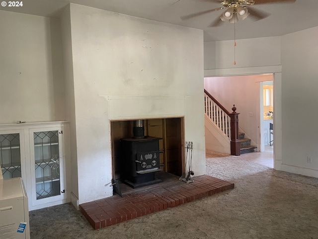 unfurnished living room featuring carpet flooring, a wood stove, and ceiling fan