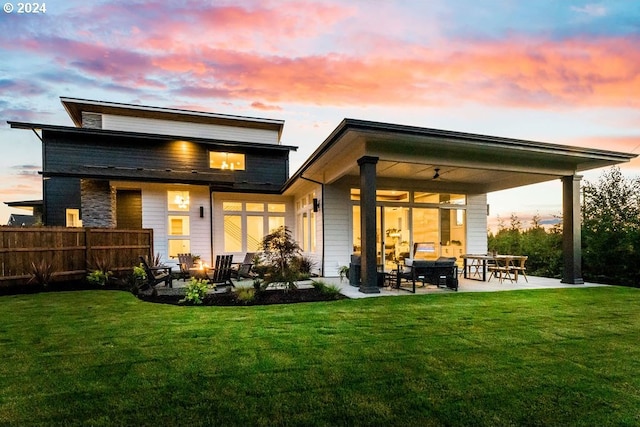 back house at dusk featuring an outdoor living space, a patio, ceiling fan, and a lawn