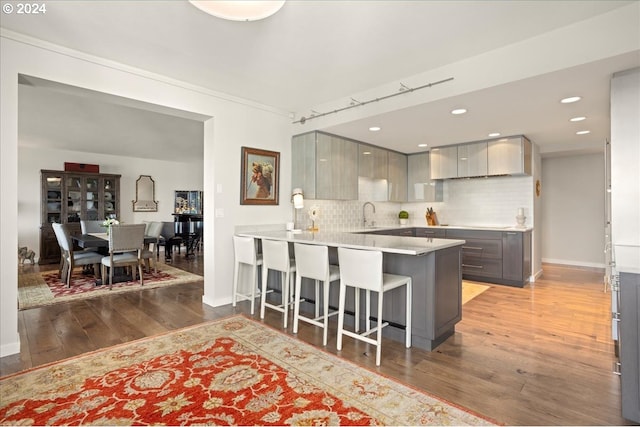 kitchen with kitchen peninsula, a kitchen breakfast bar, gray cabinetry, backsplash, and light wood-type flooring