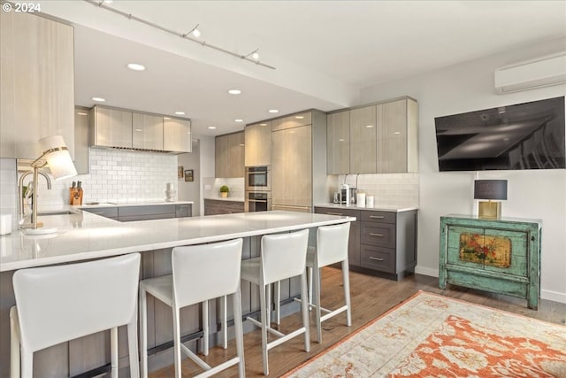 kitchen featuring a kitchen breakfast bar, sink, hardwood / wood-style flooring, decorative backsplash, and a wall unit AC