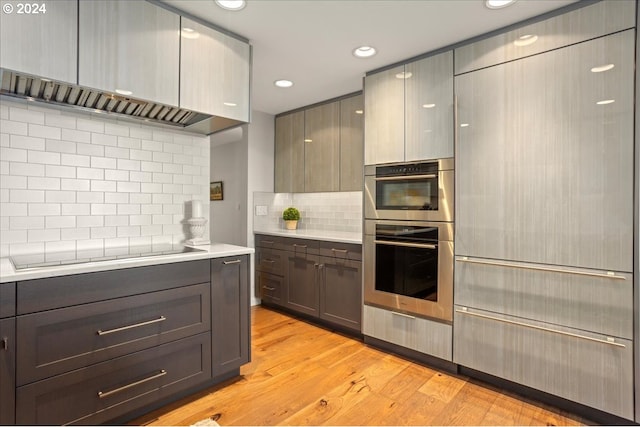 kitchen with black electric cooktop, decorative backsplash, gray cabinets, double oven, and light hardwood / wood-style flooring