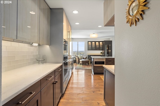 kitchen with stainless steel microwave, light hardwood / wood-style flooring, light stone counters, and backsplash