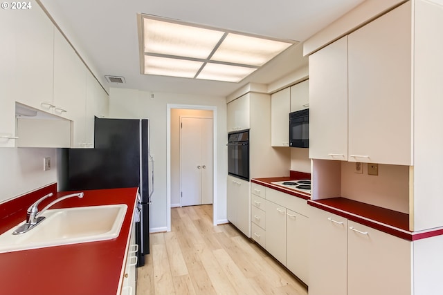 2323 SW Park Pl Unit 302, Portland, OR 97205 - kitchen with black appliances, a sink, light wood finished floors, and white cabinetry