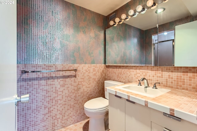 bathroom featuring tile patterned flooring, vanity, toilet, and tile walls