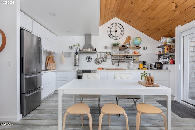 kitchen featuring lofted ceiling, white cabinets, light hardwood / wood-style flooring, wall chimney exhaust hood, and appliances with stainless steel finishes