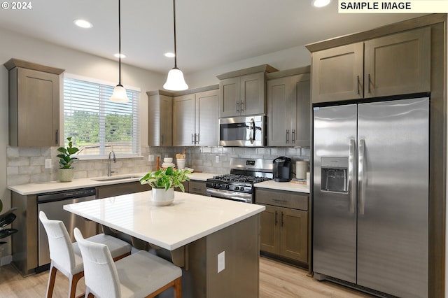 kitchen with a center island, sink, hanging light fixtures, appliances with stainless steel finishes, and light hardwood / wood-style floors