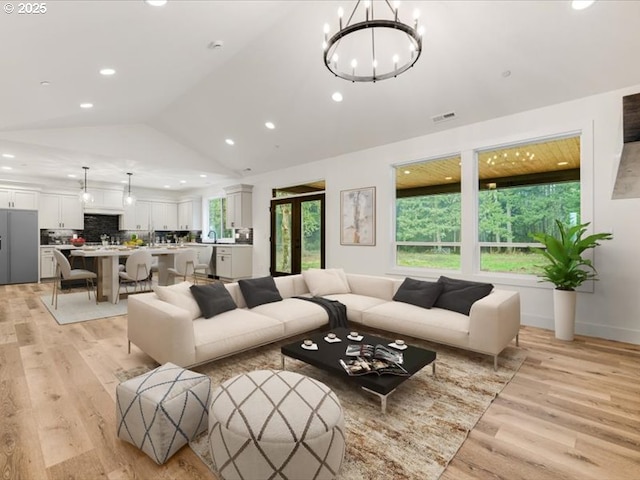 living room featuring light hardwood / wood-style floors, a notable chandelier, and vaulted ceiling