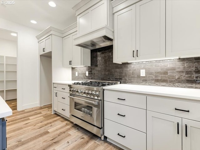 kitchen with white cabinetry, decorative backsplash, stainless steel stove, light hardwood / wood-style flooring, and custom range hood