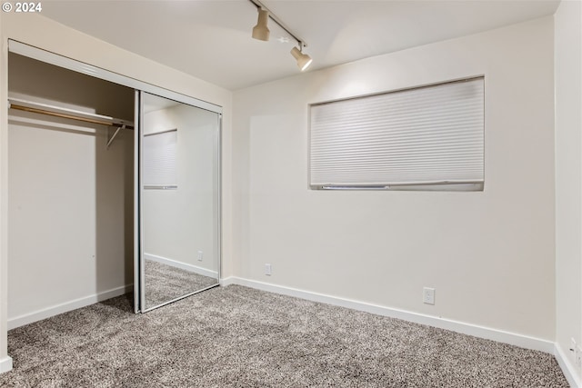 unfurnished bedroom with carpet flooring, a closet, and rail lighting