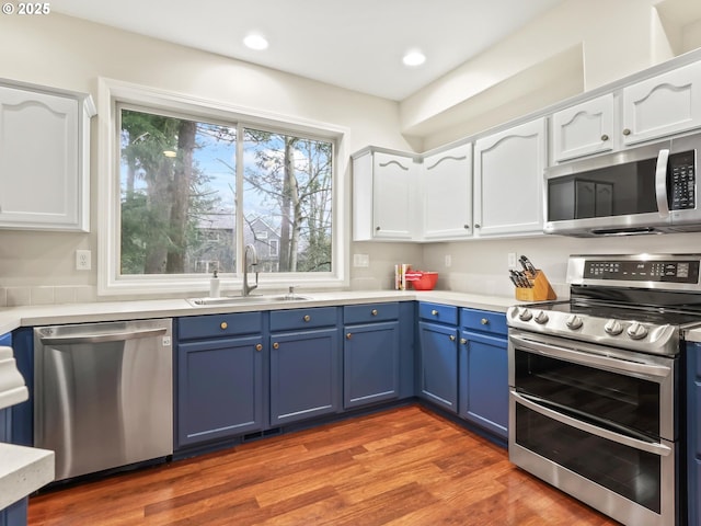 kitchen with wood-type flooring, white cabinetry, sink, blue cabinets, and stainless steel appliances