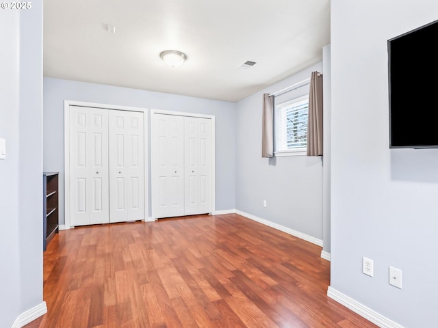 unfurnished bedroom featuring multiple closets and hardwood / wood-style floors