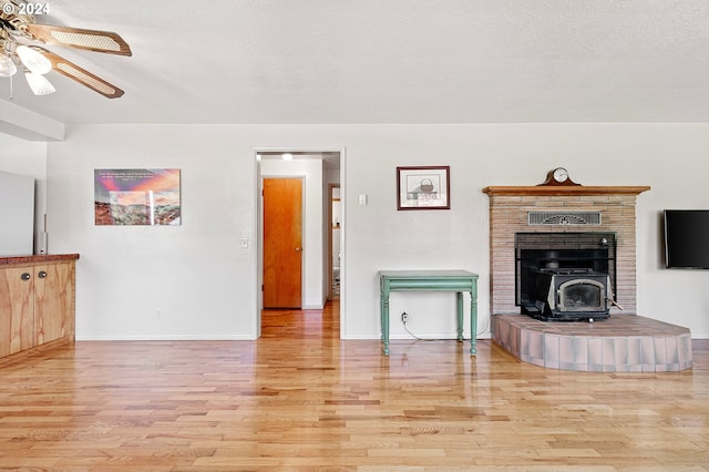 unfurnished living room featuring light hardwood / wood-style floors, a wood stove, a textured ceiling, and ceiling fan