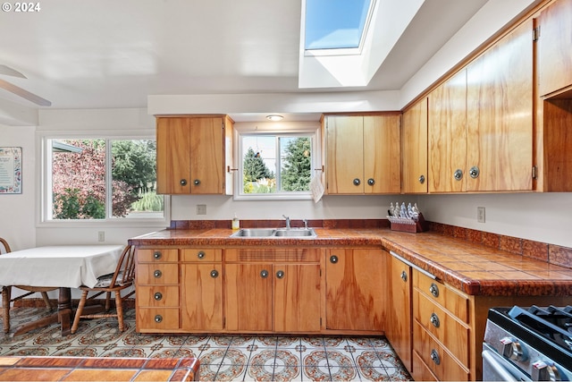 kitchen with brown cabinetry, a skylight, a sink, and stainless steel range with gas stovetop