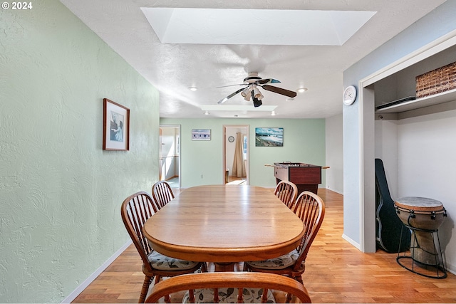 dining space featuring a textured wall, a ceiling fan, light wood finished floors, and a skylight
