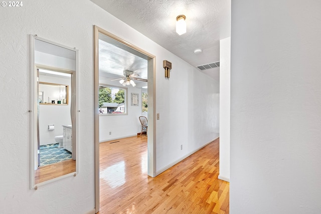 hall featuring baseboards, visible vents, light wood-type flooring, and a textured ceiling