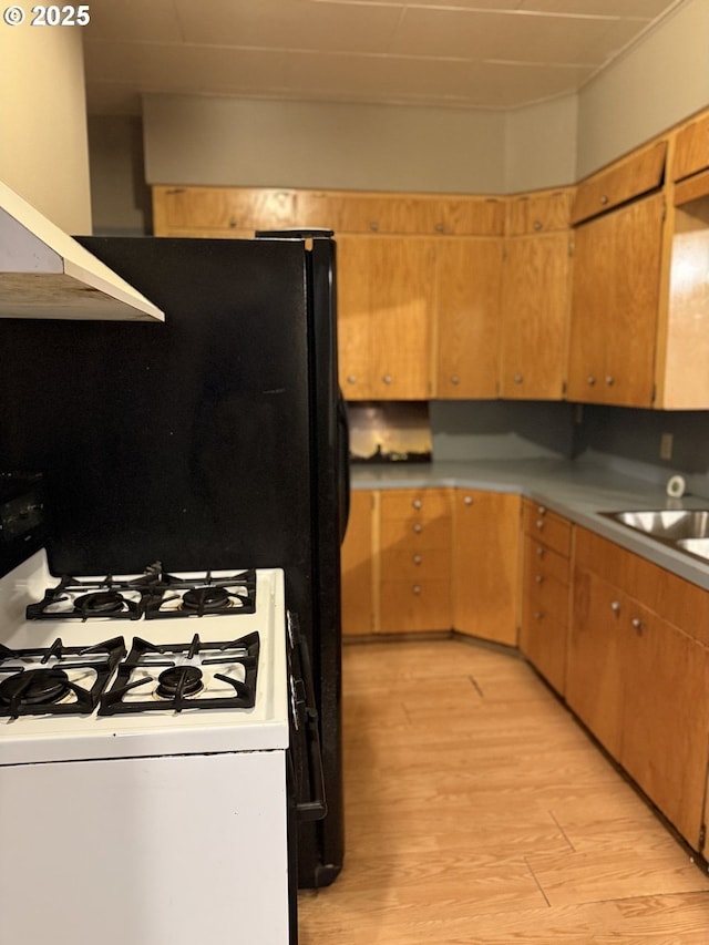 kitchen with white range with gas stovetop, light hardwood / wood-style flooring, extractor fan, and sink