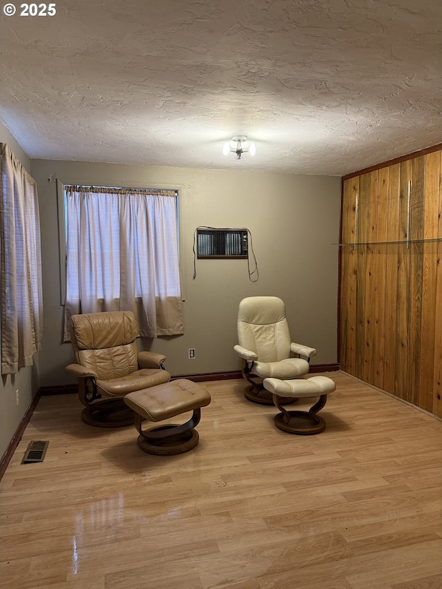 sitting room featuring a wall unit AC, wood walls, light hardwood / wood-style flooring, and a textured ceiling