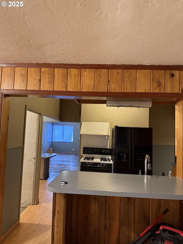 kitchen with wood walls, black refrigerator with ice dispenser, sink, white gas stove, and kitchen peninsula