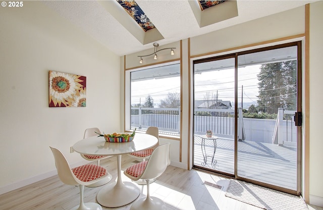 dining area featuring a skylight, light wood-style flooring, baseboards, and a textured ceiling