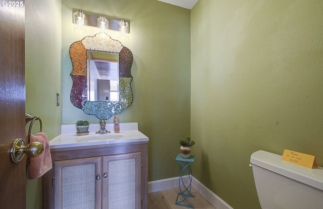 half bath with vanity, toilet, wood finished floors, and baseboards