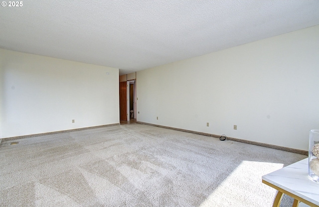 empty room featuring light colored carpet, baseboards, and a textured ceiling