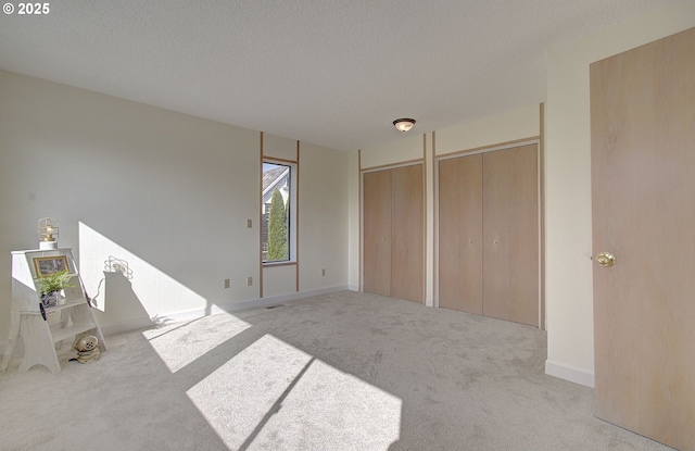 unfurnished bedroom with carpet flooring, baseboards, multiple closets, and a textured ceiling