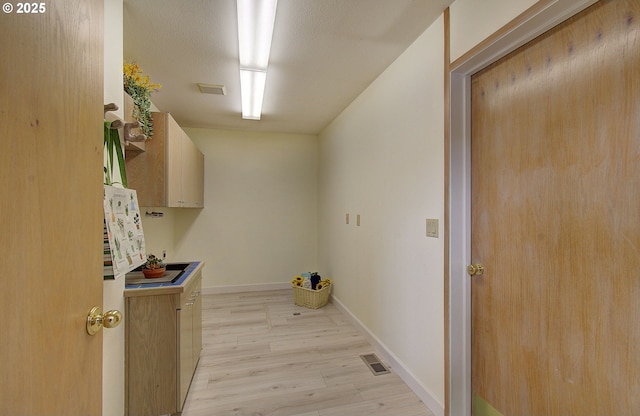 clothes washing area featuring baseboards, visible vents, and light wood finished floors