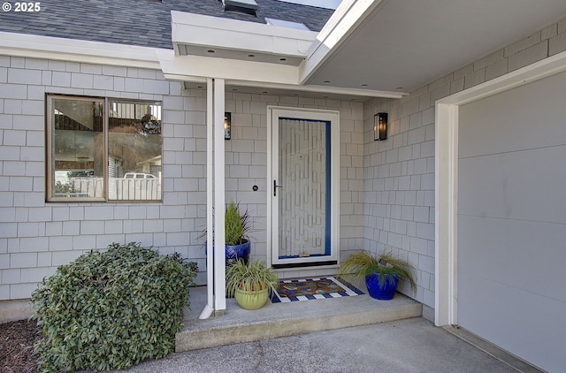 view of exterior entry with roof with shingles