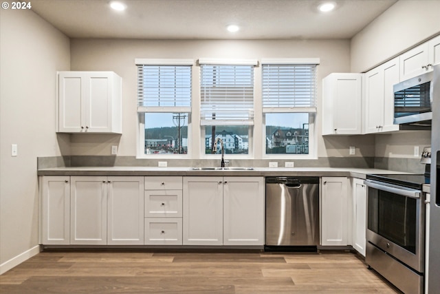 kitchen with appliances with stainless steel finishes, light hardwood / wood-style floors, white cabinetry, and a wealth of natural light