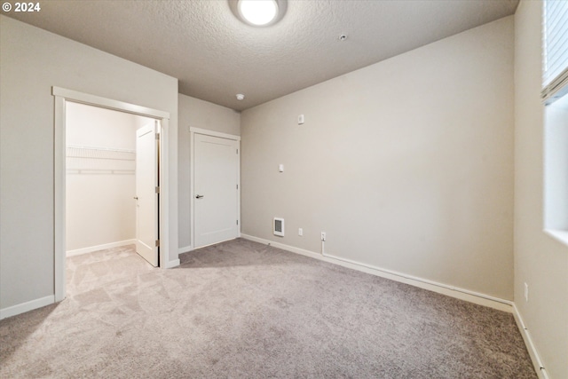 unfurnished bedroom featuring a walk in closet, light carpet, a closet, and a textured ceiling