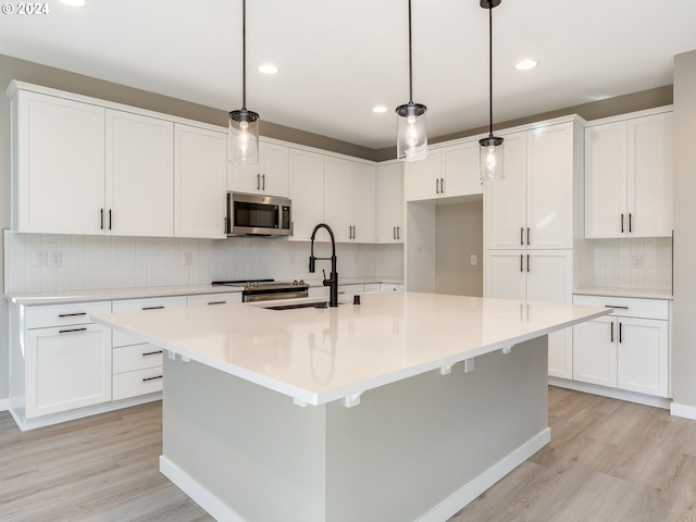 kitchen with a kitchen island with sink, white cabinets, and pendant lighting