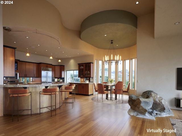 kitchen featuring built in refrigerator, a chandelier, a high ceiling, a breakfast bar area, and light hardwood / wood-style floors