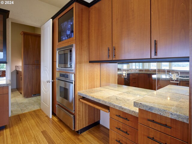 kitchen with light wood-type flooring, appliances with stainless steel finishes, built in desk, and sink