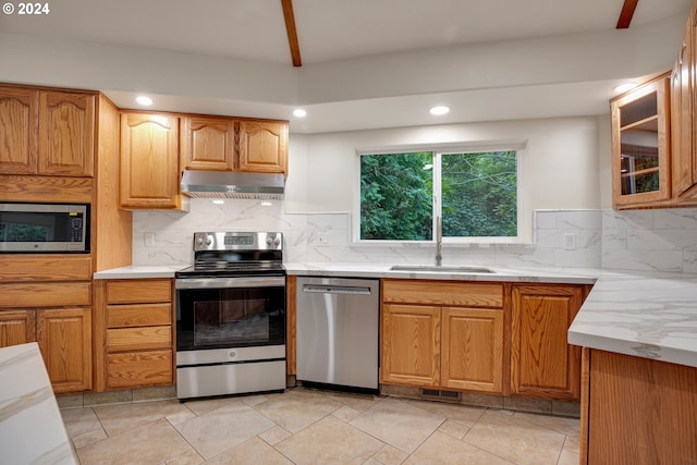 kitchen featuring light stone counters, range hood, lofted ceiling, decorative backsplash, and stainless steel appliances