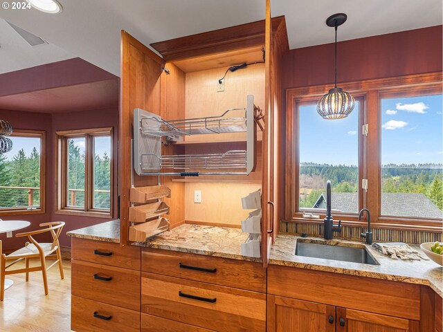 kitchen featuring light wood-type flooring, light stone counters, sink, an inviting chandelier, and hanging light fixtures