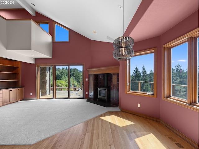 unfurnished living room featuring beam ceiling, light hardwood / wood-style flooring, a wood stove, and a notable chandelier