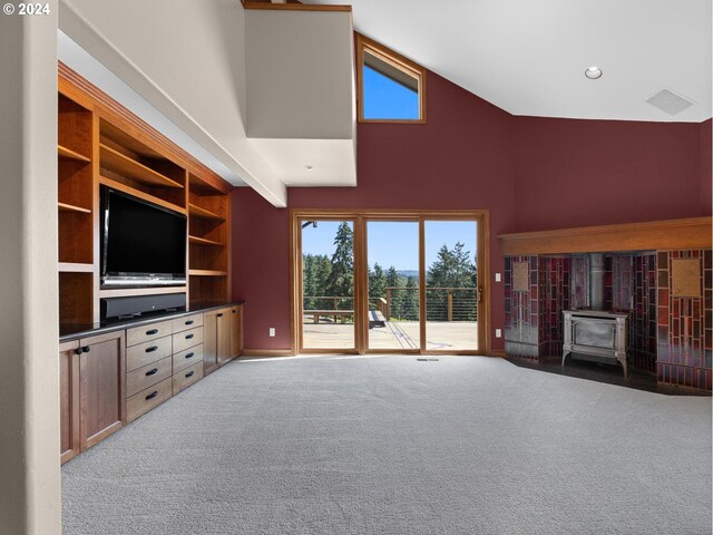 unfurnished living room with a wood stove, built in shelves, high vaulted ceiling, and light colored carpet