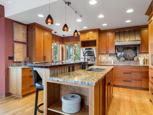 kitchen with decorative backsplash, a center island with sink, and light stone counters