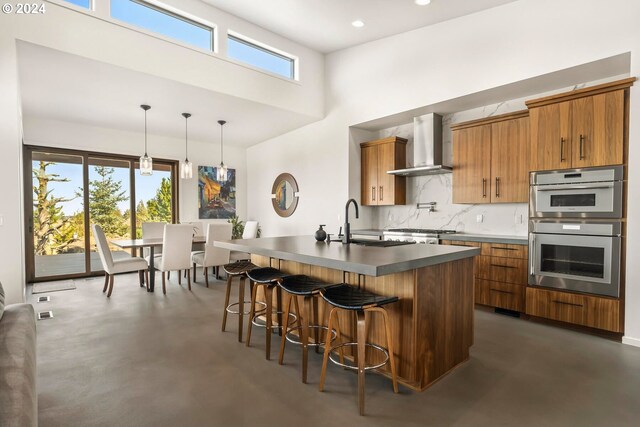 kitchen featuring a wealth of natural light, stainless steel double oven, and wall chimney exhaust hood