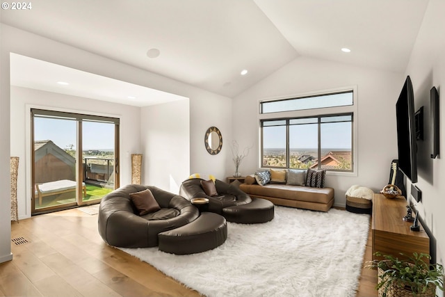 living room with a wealth of natural light, vaulted ceiling, and light hardwood / wood-style flooring